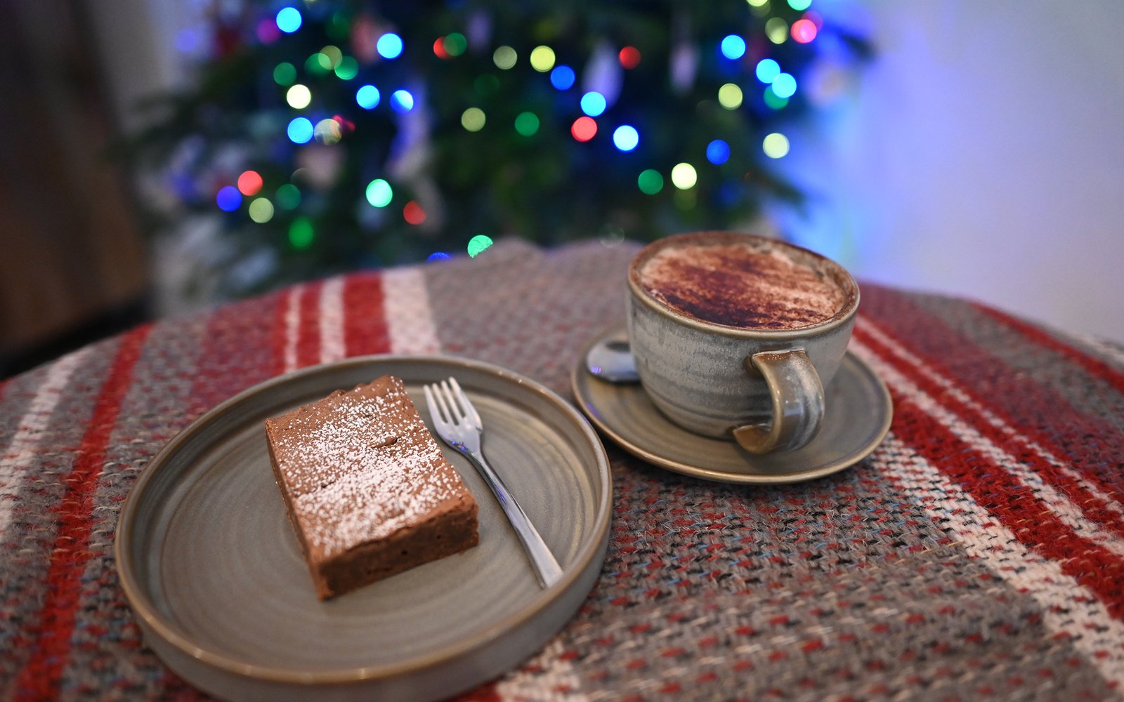 Cup of hot chocolate and a brownie with illuminated christmas tree in background