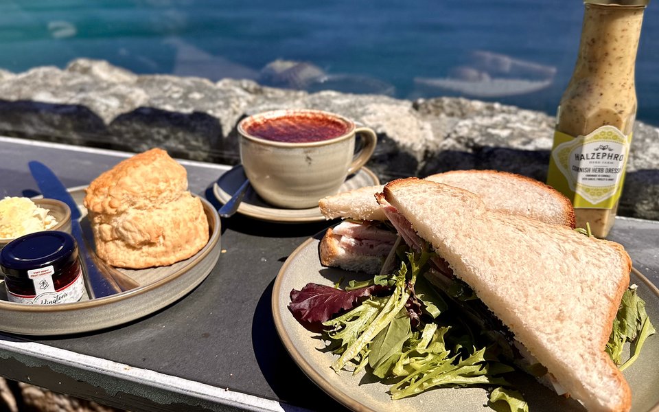 Sandwich and cream tea on a ledge in the cafe with sea in background.